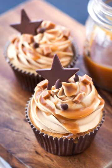 2 Salted Caramel Almond Cupcakes on a dark wooden surface.