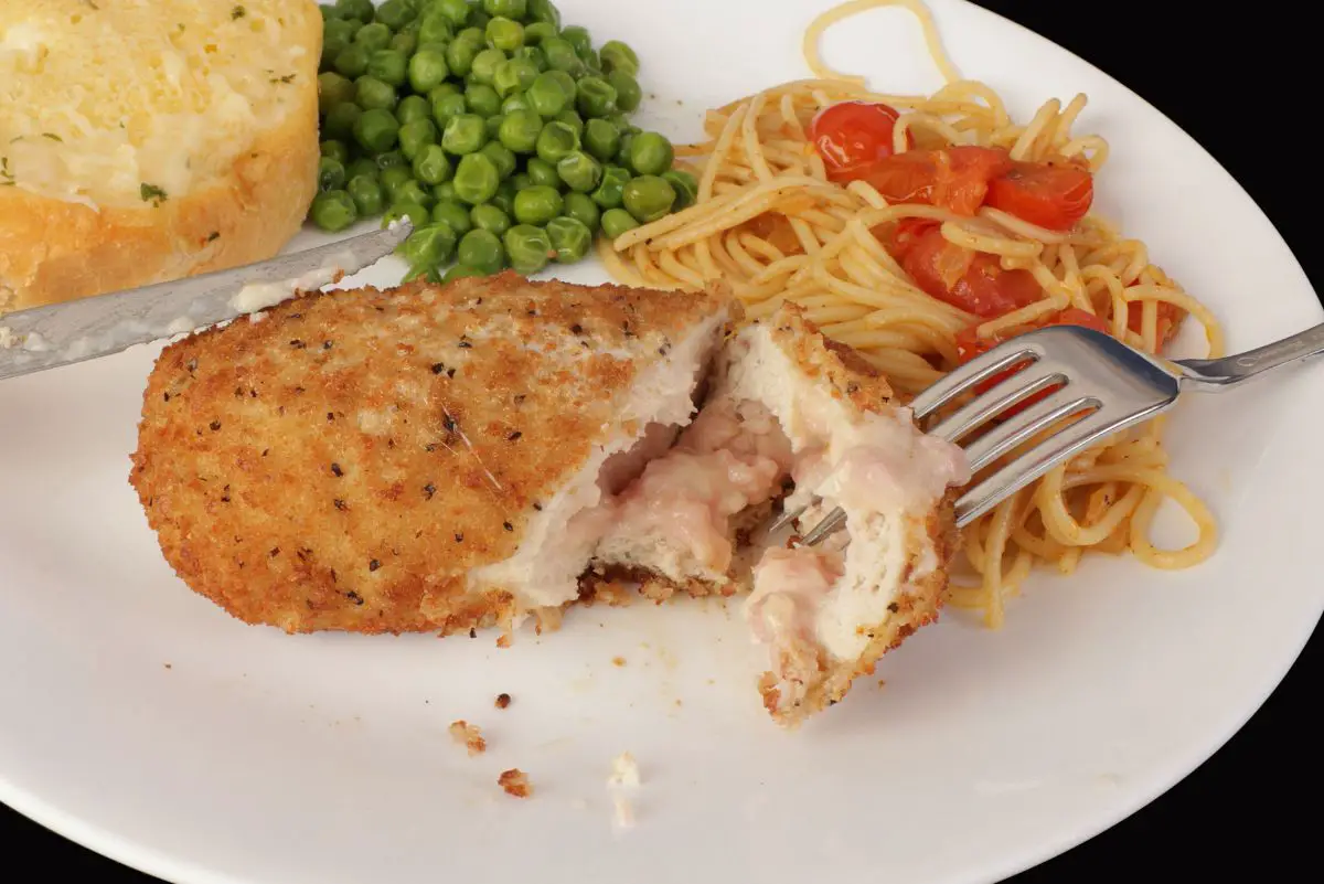 Chicken Cordon Bleu on a white plate with peas, spaghetti, and bread.