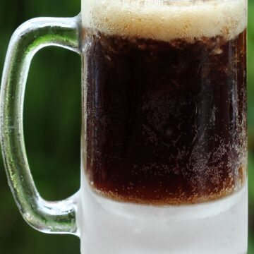 Closeup of 5 Ingredient Homemade Root Beer in a clear glass mug, an out of focus green background.