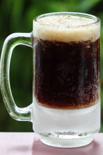 Closeup of 5 Ingredient Homemade Root Beer in a clear glass mug, an out of focus green background.