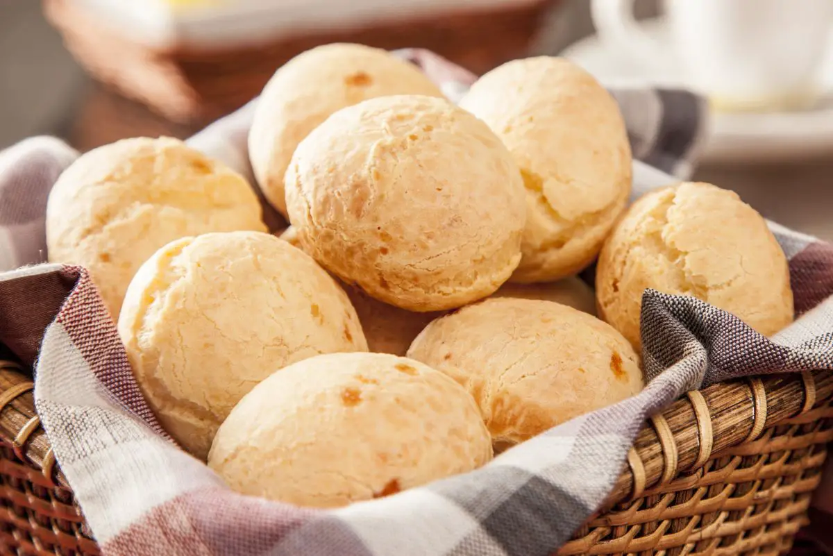 Homemade Brazilian Cheese Bread rolls in a basket lined with a gray and white checked cloth.