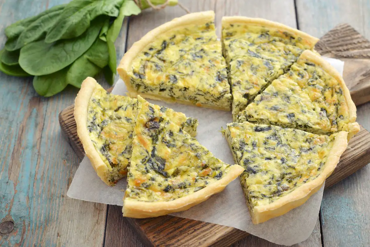 Sliced Easy Spinach Green Chile Quiche on a wooden cutting board.