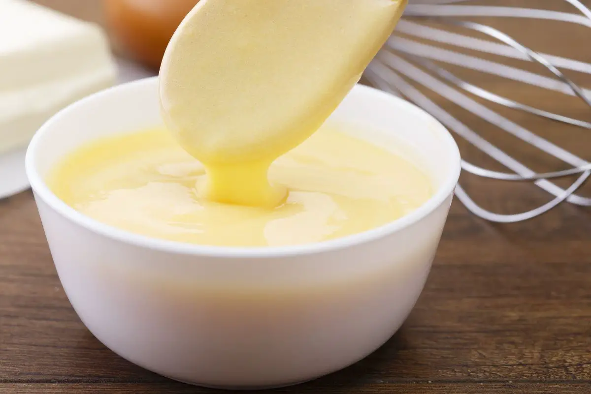 Quick and Easy Hollandaise Sauce in a white bowl with a wooden spoon.