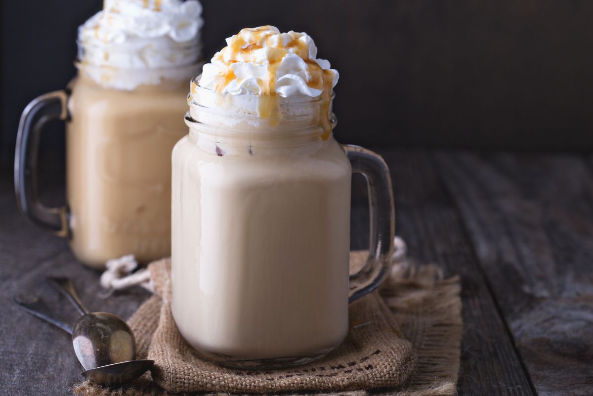 2 Copycat Starbucks Caramel Frappuccinos in clear glass jars on a rustic, wooden surface.