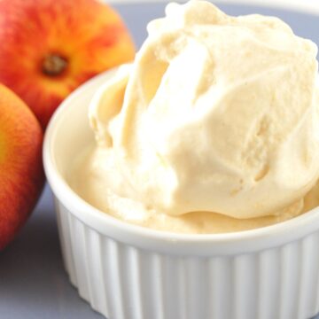 Closeup of Homemade Peach Ice Cream in a white rameken with fresh peaches behind it.