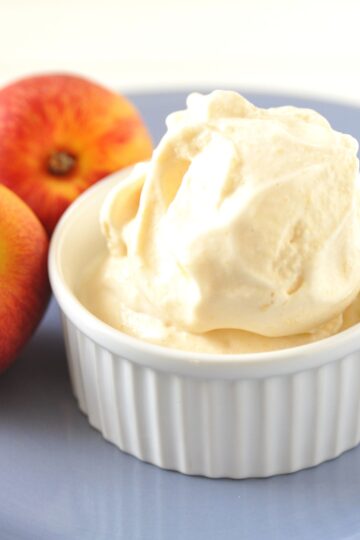 Closeup of Homemade Peach Ice Cream in a white rameken with fresh peaches behind it.