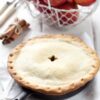 Easy Skillet Apple Pie on a white table cloth with a basket of apples, and a bunch of cinnamon sticks behind it.