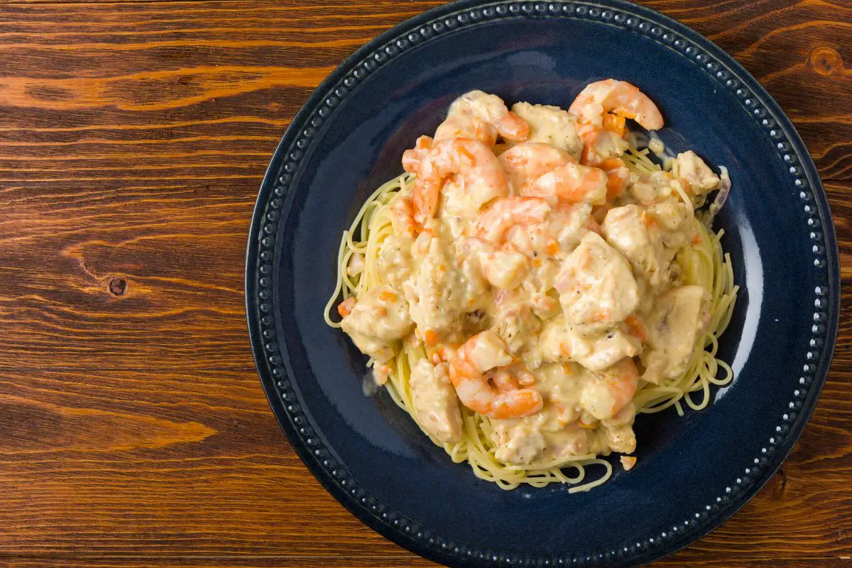 Overhead view of Olive Garden Chicken and Shrimp Carbonara on a dark plate sitting on a wooden surface.