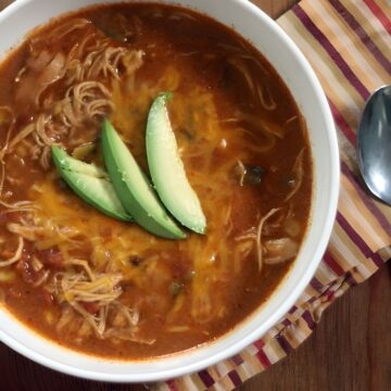 Overhead view of Copycat Chicken Enchilada Soup (Chili's) in a white bowl garnished with sliced avocado.