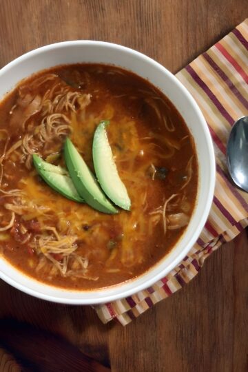 Overhead view of Copycat Chicken Enchilada Soup (Chili's) in a white bowl garnished with sliced avocado.