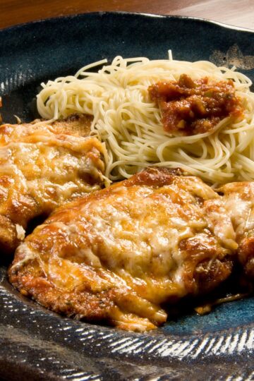 Closeup of Mouth-Watering Mozzarella & Parmesan Chicken no a black plate.