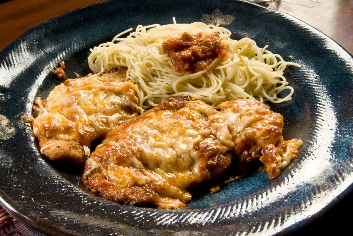 Mouth-Watering Mozzarella & Parmesan Chicken on a black plate with spaghetti.