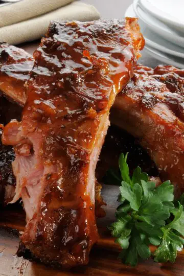 Glazed baby back ribs on a cutting board with a side of parsley, ready for serving.
