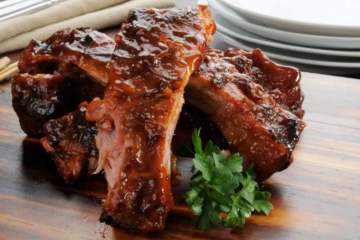 Juicy baby back ribs coated in barbecue sauce on a wooden surface, garnished with fresh parsley.