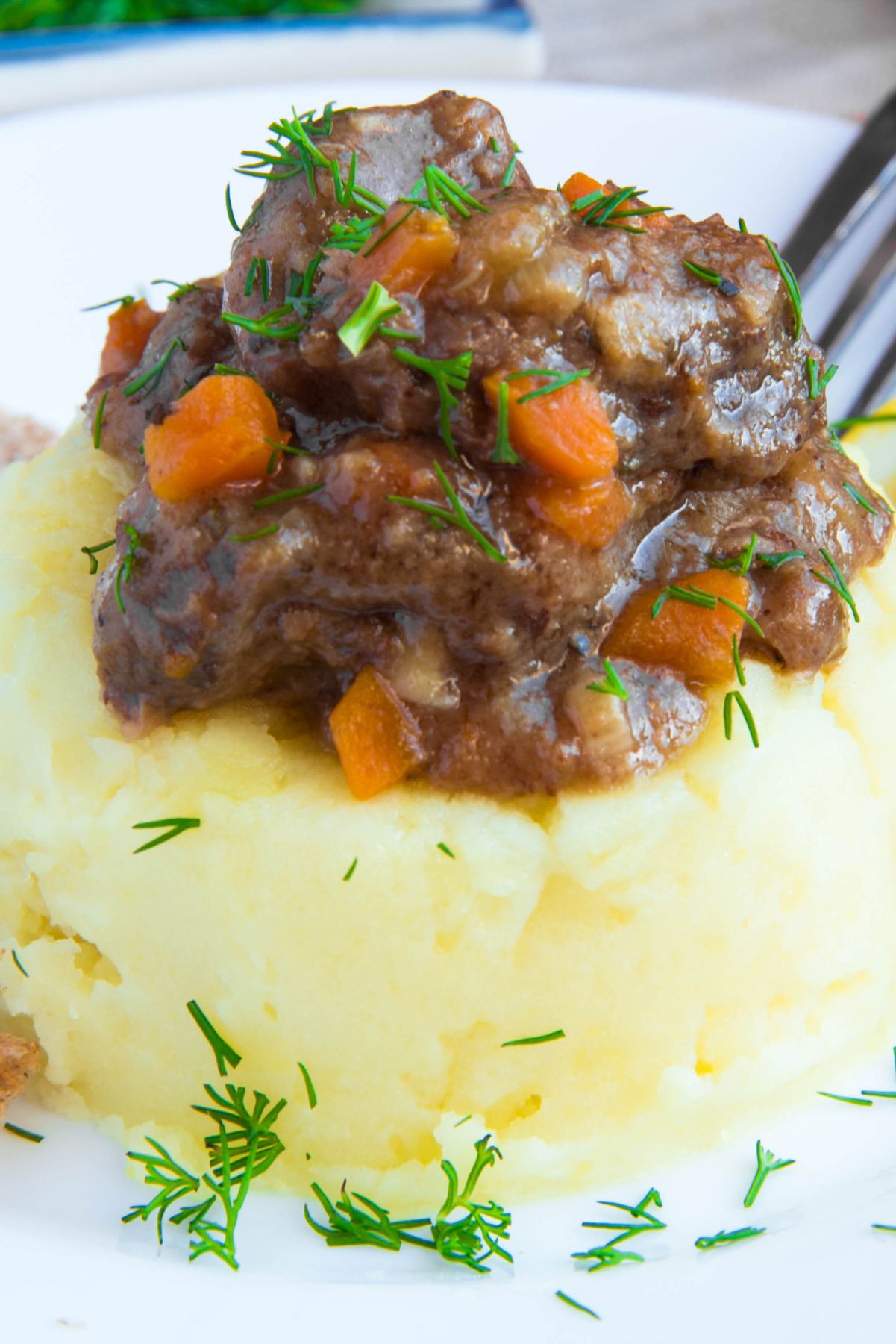 Traditional Irish beef stew atop creamy mashed potatoes, with fresh herbs on top, a slice of lemon to the side, and brown bread arranged on a white plate.