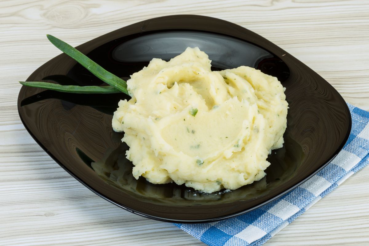 Irish Champ mashed potatoes garnished with green onion on a dark plate with a blue and white checked napkin, ready to be served.