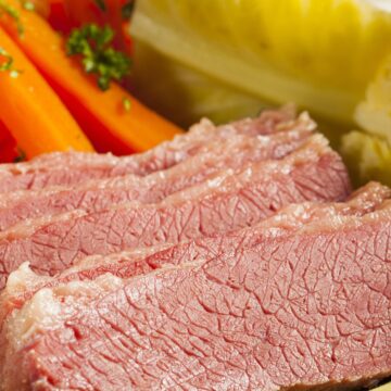 A plate of Irish corned beef sliced thin, accompanied by steamed cabbage wedges, whole carrots, and red potatoes, garnished with parsley