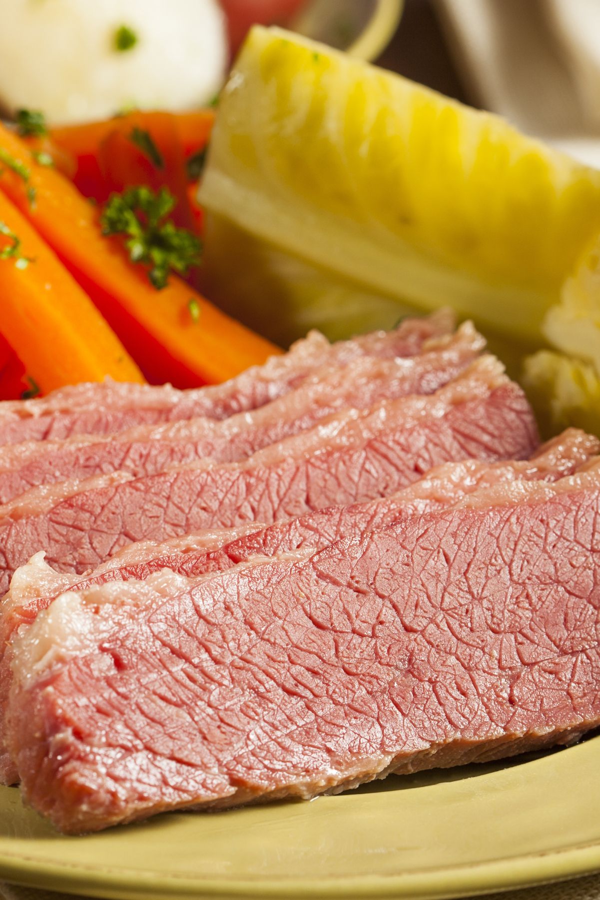 A plate of Irish corned beef sliced thin, accompanied by steamed cabbage wedges, whole carrots, and red potatoes, garnished with parsley