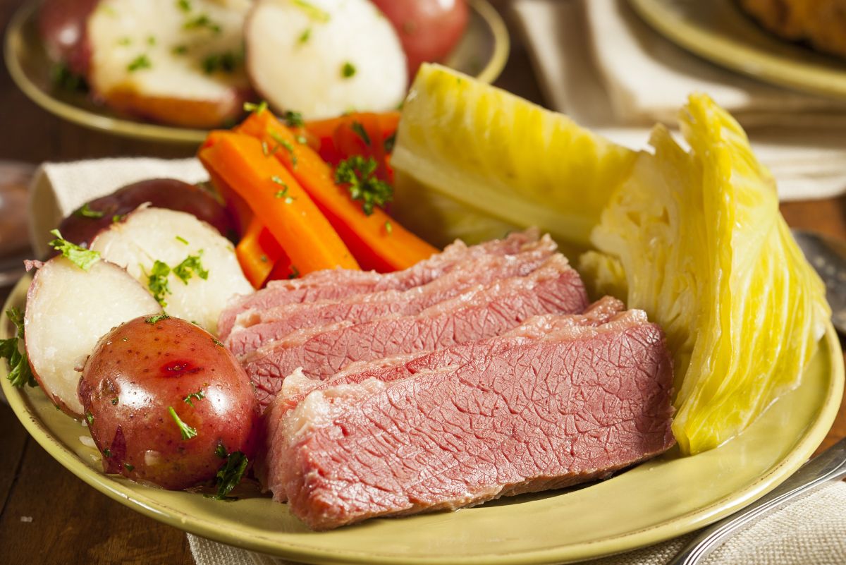 Traditional Irish dinner of sliced corned beef with a side of cabbage, carrots, and potatoes on a ceramic plate, ready to be enjoyed.