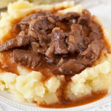A plate of traditional Irish stew made with tender beef, simmering in a dark Guinness gravy, atop fluffy mashed potatoes, presented on a decorative white dish with intricate patterns.