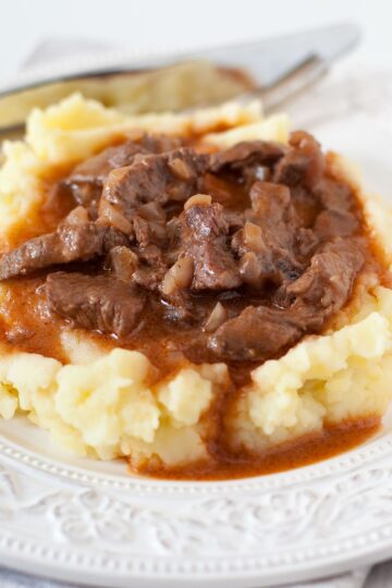 A plate of traditional Irish stew made with tender beef, simmering in a dark Guinness gravy, atop fluffy mashed potatoes, presented on a decorative white dish with intricate patterns.
