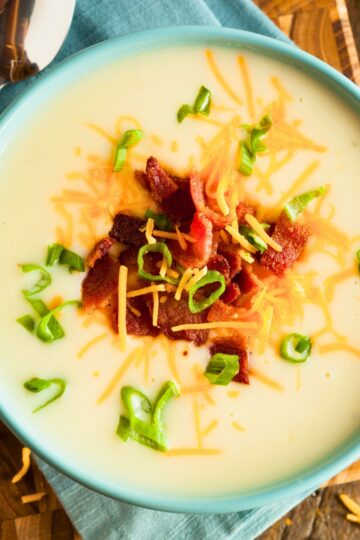 Creamy baked potato soup served in a blue bowl, topped with crispy bacon pieces, shredded cheddar cheese, and fresh chopped green onions for a hearty and comforting dish.