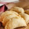 Golden brown cinnamon apple hand pies with flaky crust sprinkled with coarse sugar, arranged on parchment paper. These handheld desserts have a crimped edge and a rustic, homemade look, perfect for fall baking or a sweet treat.