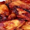 Close-up of baked chicken wings piled on a white platter, coated in a sticky garlic honey sriracha glaze with glossy red sauce and caramelized edges. Golden-brown, juicy skin; spicy-sweet baked chicken wings appetizer, perfect for game day.