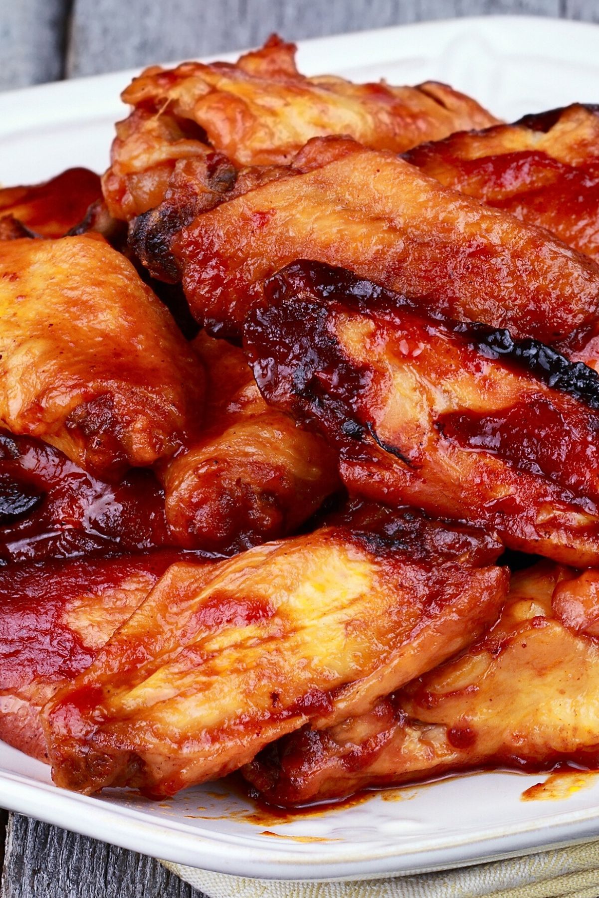 Close-up of baked chicken wings piled on a white platter, coated in a sticky garlic honey sriracha glaze with glossy red sauce and caramelized edges. Golden-brown, juicy skin; spicy-sweet baked chicken wings appetizer, perfect for game day.