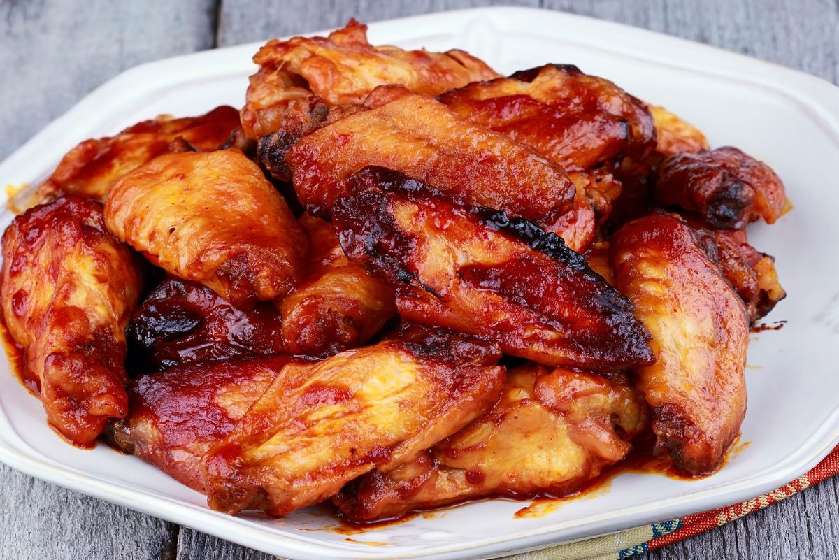 Pile of baked chicken wings on a white platter, coated in a glossy garlic honey sriracha sauce with caramelized edges and golden skin; spicy-sweet baked chicken wings appetizer on a rustic wood table.
