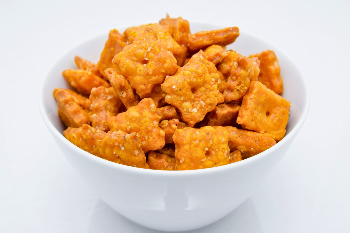 White bowl filled with homemade copycat Cheez-It crackers, baked to a golden orange with a crisp texture and sprinkled with coarse salt. The square cheddar crackers have small center holes and a crunchy, cheesy coating, making them a close match to the classic snack.