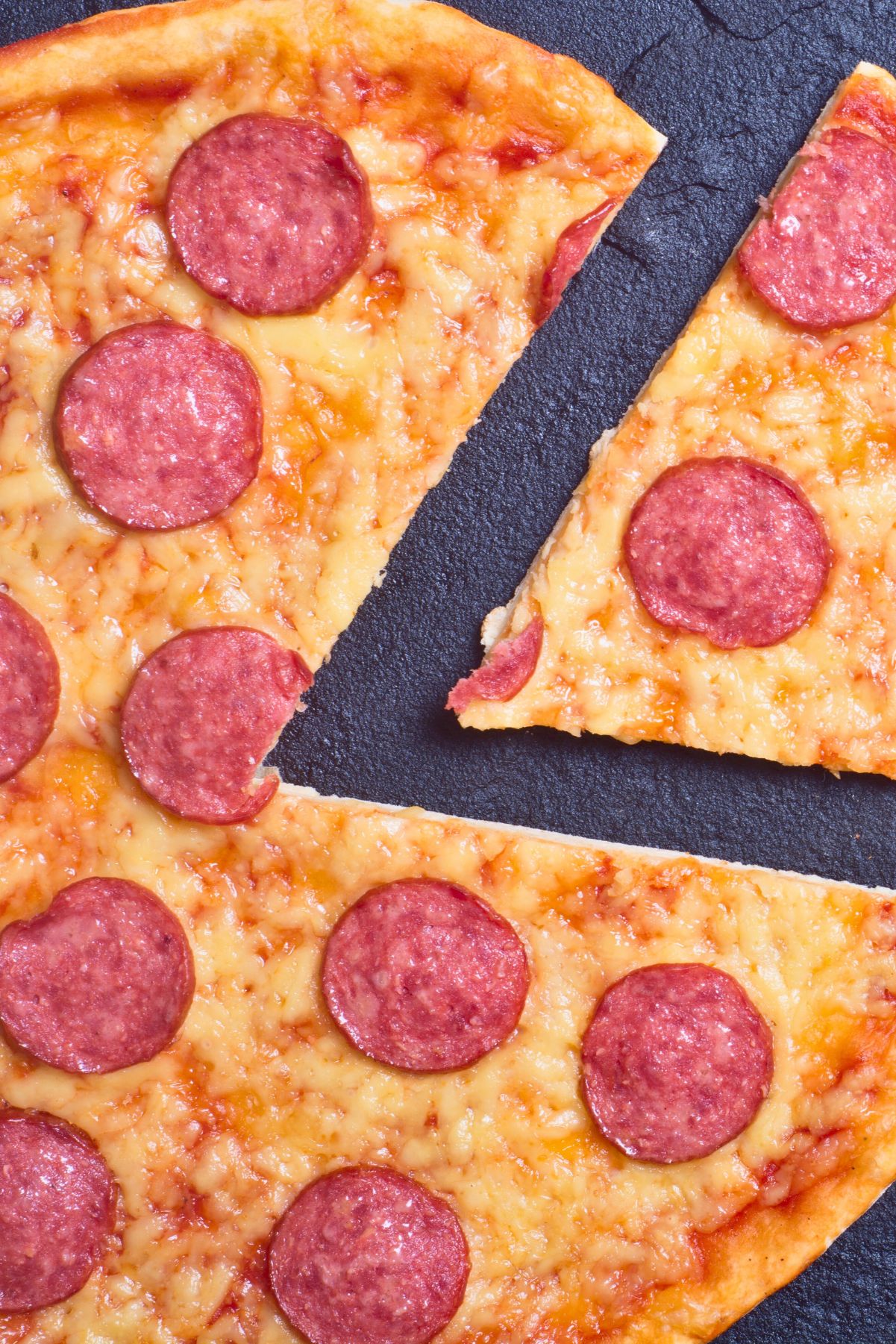 Close-up of a New York style pepperoni pizza with a thin, golden crust and melted cheese. One slice is pulled slightly away, showing the crispy edge and stretchy cheese, highlighting the classic pizzeria look.