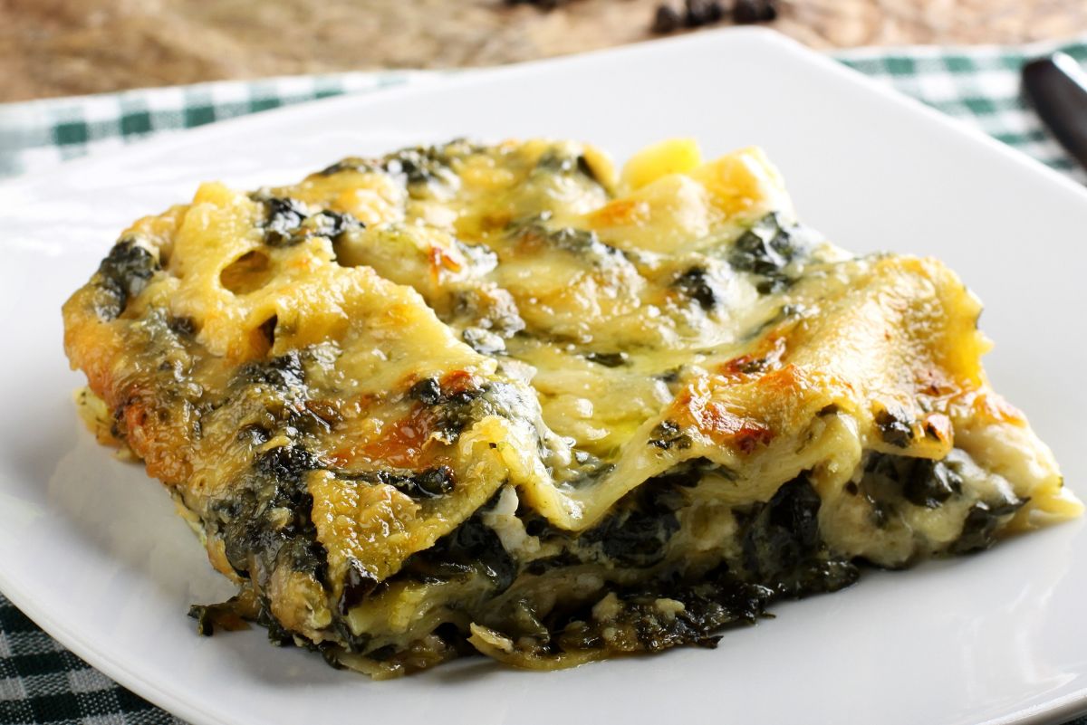 Golden, cheesy Chicken Alfredo Lasagna with Spinach served on a white plate over a green plaid napkin. Layers of tender noodles, creamy Alfredo sauce, chicken, and spinach baked to a bubbling finish. Comfort food, creamy pasta casserole, Italian-inspired dinner.