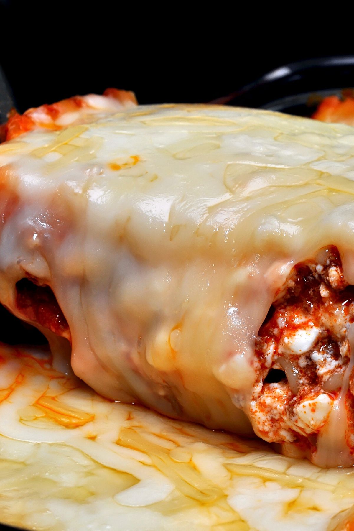 Close-up of Cozy Baked Mexican Lasagna in a casserole dish, a thick blanket of melted cheese over layered tortillas with red salsa-tomato meat sauce and cottage cheese curds visible. Cheesy baked casserole, Mexican lasagna recipe, easy weeknight dinner.