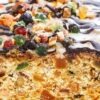 Close-up of old-fashioned white Christmas fruitcake, golden crumb packed with candied fruit and nuts, topped with colorful candied pieces and a glossy chocolate drizzle in a white pan. Holiday dessert recipe, fruitcake.