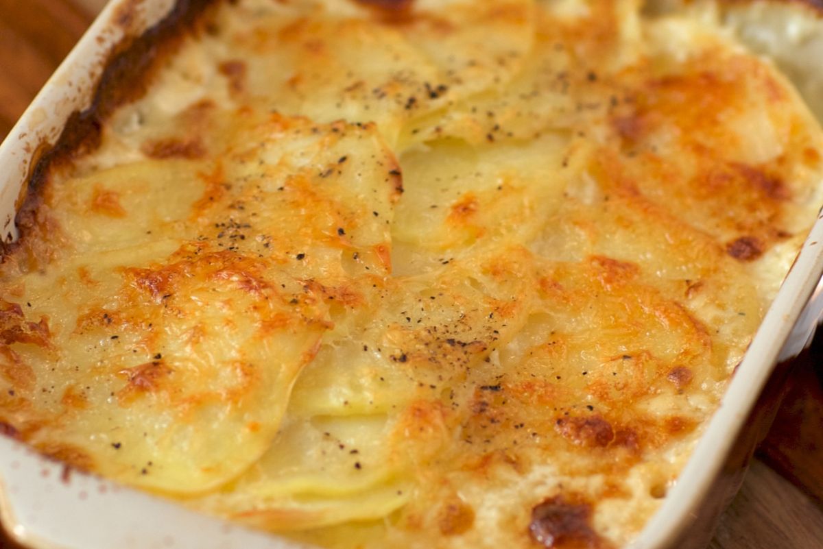 Creamy Alfredo potato lasagna baked in a white dish, topped with golden melted cheese and specks of black pepper. Thinly sliced potatoes are layered in a rich, cheesy sauce with lightly browned edges, creating a warm and comforting homemade look.