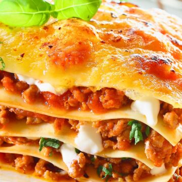 Cheesy beef lasagna with golden bubbly top, stacked pasta layers, rich meat sauce, creamy ricotta, and fresh basil on top.