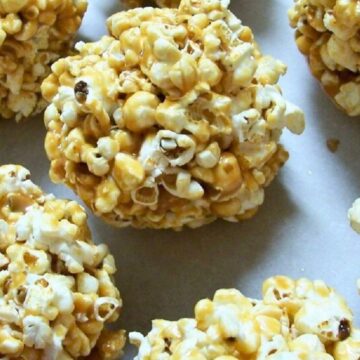 Golden caramel popcorn balls arranged on a white surface. Popped corn coated in sticky caramel, formed into round snack balls with a crunchy texture. Close-up food photography showing glossy caramel and fluffy popcorn pieces.