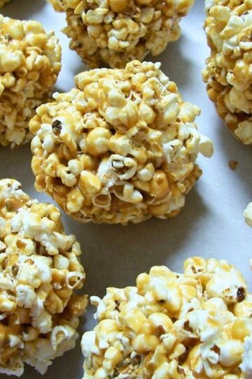 Golden caramel popcorn balls arranged on a white surface. Popped corn coated in sticky caramel, formed into round snack balls with a crunchy texture. Close-up food photography showing glossy caramel and fluffy popcorn pieces.