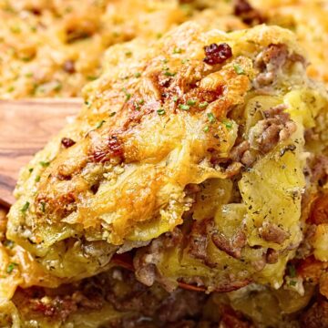 Close-up of ground beef and potato bake layered with thin sliced potatoes, seasoned beef, and melted cheddar cheese. Golden brown cheesy crust with crispy edges, a generous square lifted from a black baking dish on a wooden spatula. Hearty comfort food casserole dinner.