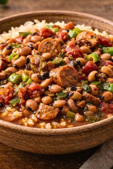 Southern black eyed pea gumbo served over white rice in a rustic bowl. Hearty crockpot stew with sliced sausage, black eyed peas, diced tomatoes, green bell peppers, and herbs in a rich savory broth. Comfort food Southern dinner recipe with smoky sausage and beans.