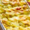 Garlic potato bake with bacon and cabbage in a white ceramic casserole dish, layered thin sliced potatoes baked until tender and topped with melted, lightly browned cheese. Creamy sauce bubbles around the edges with golden, crispy corners, served as a hearty comfort food side dish.