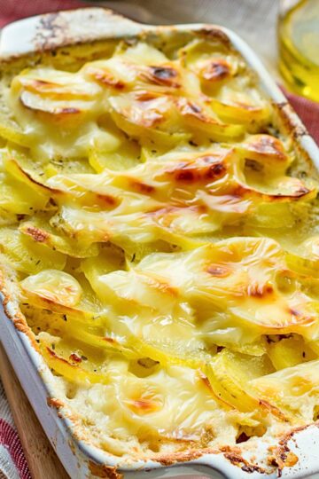 Garlic potato bake with bacon and cabbage in a white ceramic casserole dish, layered thin sliced potatoes baked until tender and topped with melted, lightly browned cheese. Creamy sauce bubbles around the edges with golden, crispy corners, served as a hearty comfort food side dish.