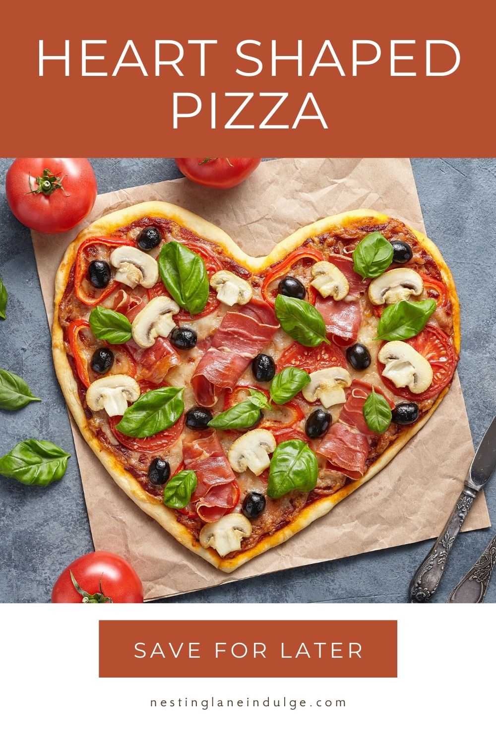 Heart shaped pizza on parchment paper topped with prosciutto, sliced mushrooms, black olives, tomato slices, melted cheese, and fresh basil leaves. Whole tomatoes around the pizza on a gray surface. Text at top reads &ldquo;Heart Shaped Pizza&rdquo; and text at bottom reads &ldquo;Save for Later&rdquo; with nestinglaneindulge.com.