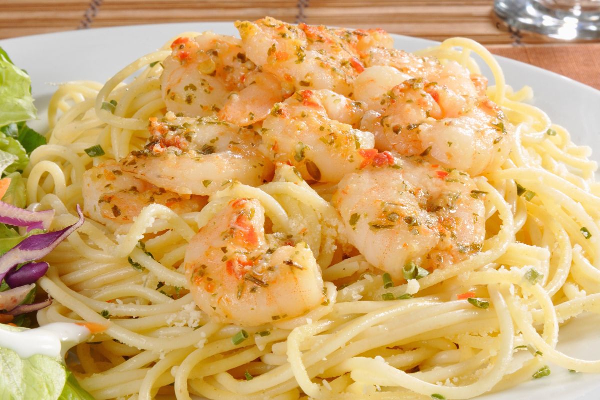 Plate of shrimp scampi served over spaghetti with garlic butter lemon sauce, herbs, and red pepper flakes, sprinkled with Parmesan. Tender shrimp on a bed of pasta with a side salad. High protein shrimp scampi recipe, easy seafood pasta dinner idea.