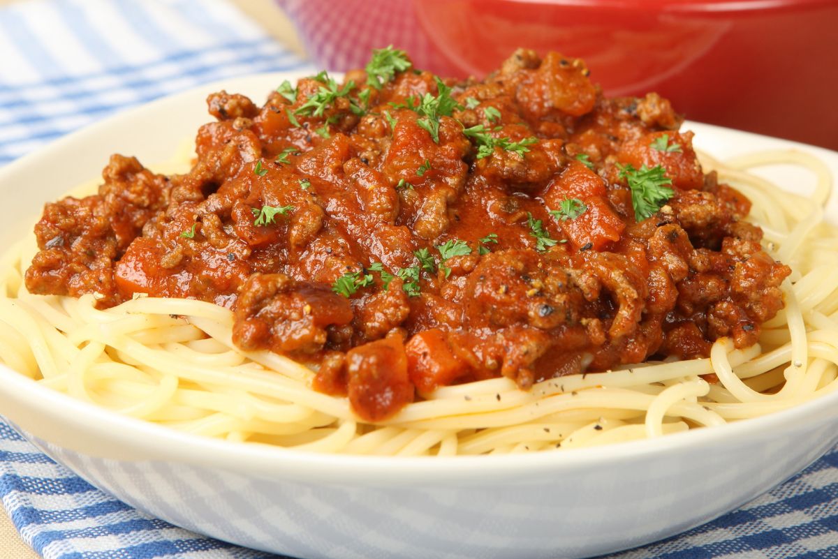 Plate of spaghetti topped with hearty Italian sausage tomato sauce and diced tomatoes, garnished with fresh chopped parsley. Rich red marinara with browned sausage over tender pasta in a white bowl. Classic high protein Italian pasta dinner, comforting family meal idea.