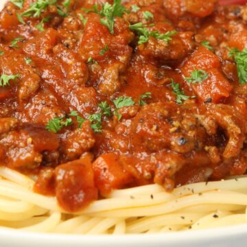 Close-up of Italian sausage pasta dinner with spaghetti topped in chunky tomato sauce, browned Italian sausage, diced tomatoes, and fresh chopped parsley. Rich red marinara over tender pasta in a white bowl. Hearty high protein pasta recipe, classic comfort food family dinner.