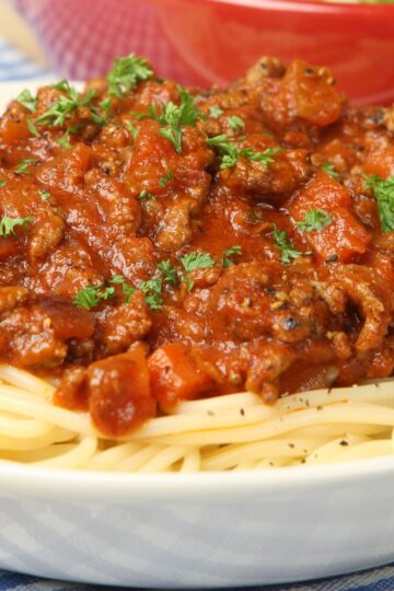 Close-up of Italian sausage pasta dinner with spaghetti topped in chunky tomato sauce, browned Italian sausage, diced tomatoes, and fresh chopped parsley. Rich red marinara over tender pasta in a white bowl. Hearty high protein pasta recipe, classic comfort food family dinner.