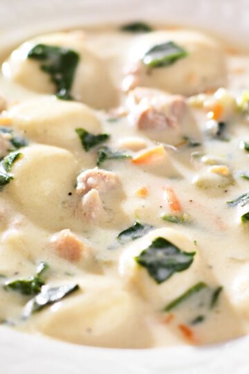 Creamy chicken gnocchi soup with tender potato gnocchi, chunks of chicken, carrots, and fresh spinach in a rich white broth. Close-up of a hearty Italian-style soup similar to Olive Garden Chicken Gnocchi Soup, thick and velvety with visible herbs and vegetables in a white bowl.