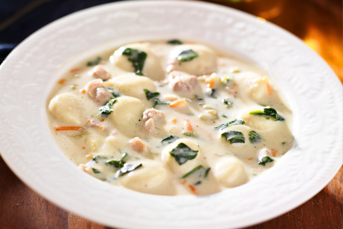 Bowl of creamy chicken gnocchi soup with soft potato gnocchi, diced chicken, carrots, and fresh spinach in a rich white broth. Hearty Italian-style comfort food similar to Olive Garden Chicken Gnocchi Soup, served in a white bowl on a wooden table.